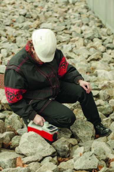 Geoscientist holding RS-225 Super-SPEC Handheld Gamma-Ray Spectrometer near a rock formation